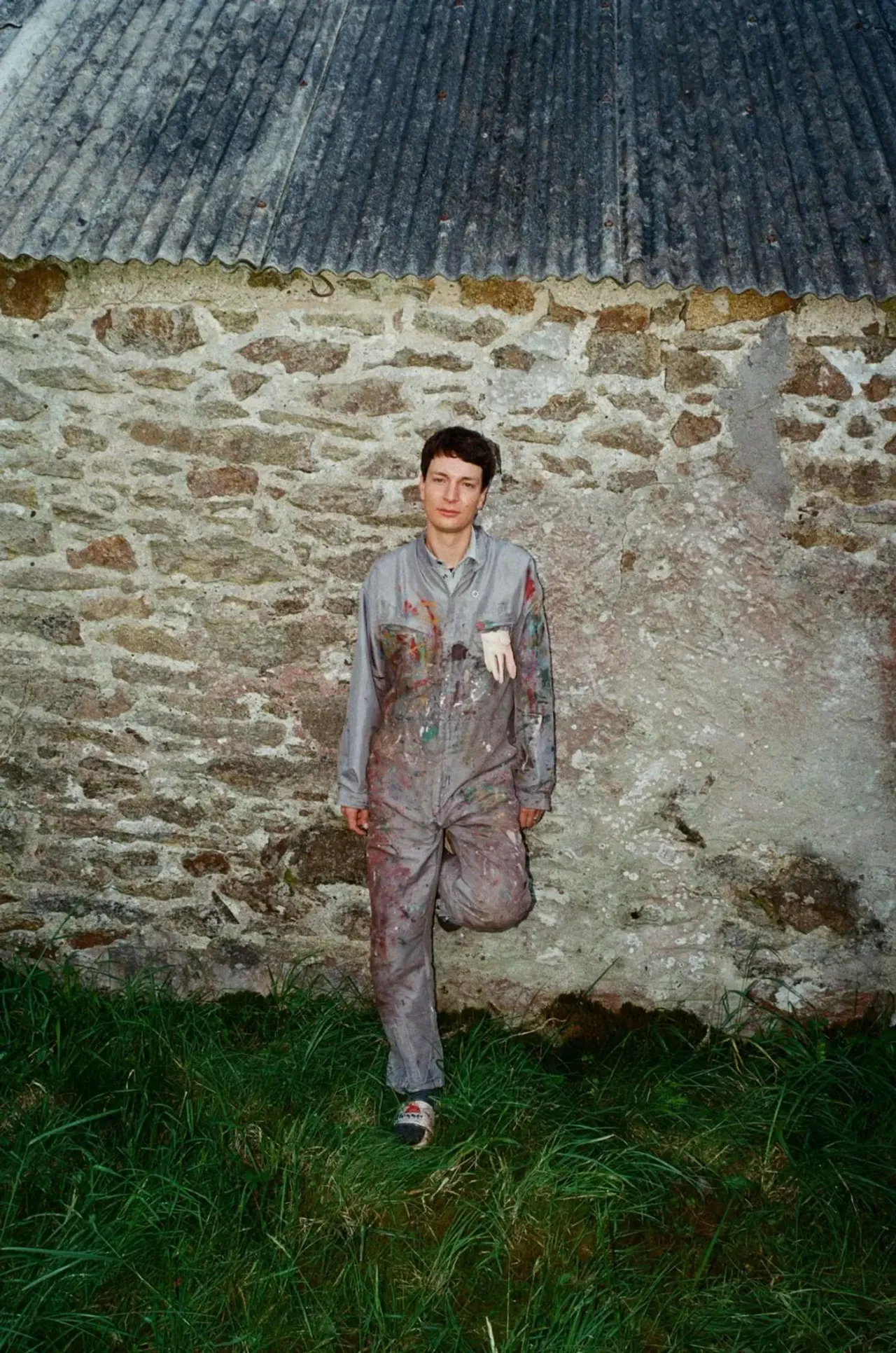 Portrait of Ruben Einsmann standing outdoors in paint-covered work clothes in front of a stone wall.