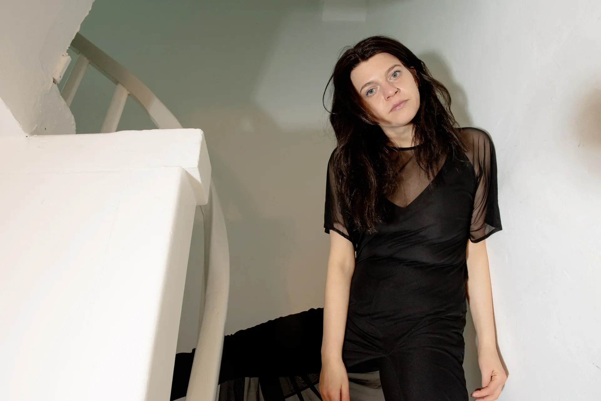 Portrait of Nadine Karl standing beside a sculptural installation in a gallery space, wearing a black top, shown in relation to her work.