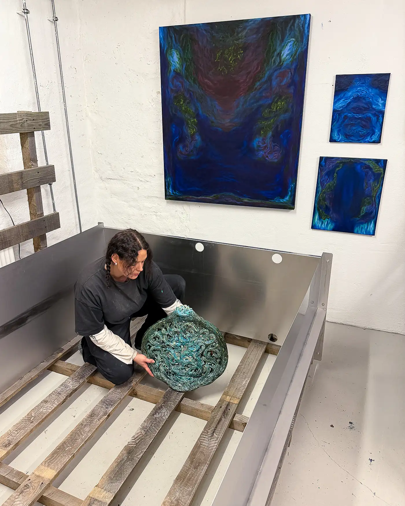 Artist Sofie Ehrhorn in her studio handling a glazed ceramic sculpture, surrounded by blue abstract paintings on the wall