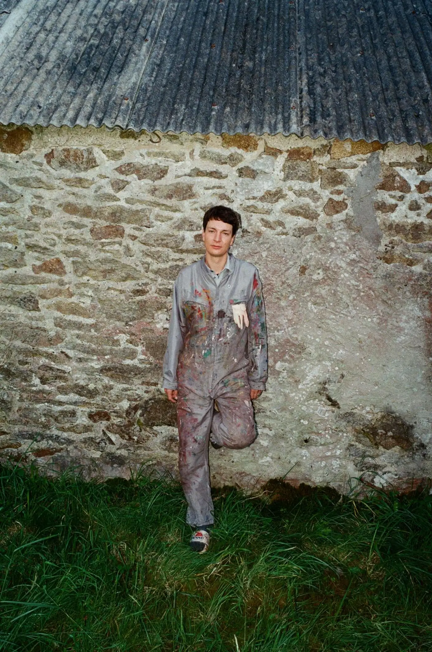 Portrait of Ruben Einsmann standing outdoors in paint-covered work clothes in front of a stone wall.