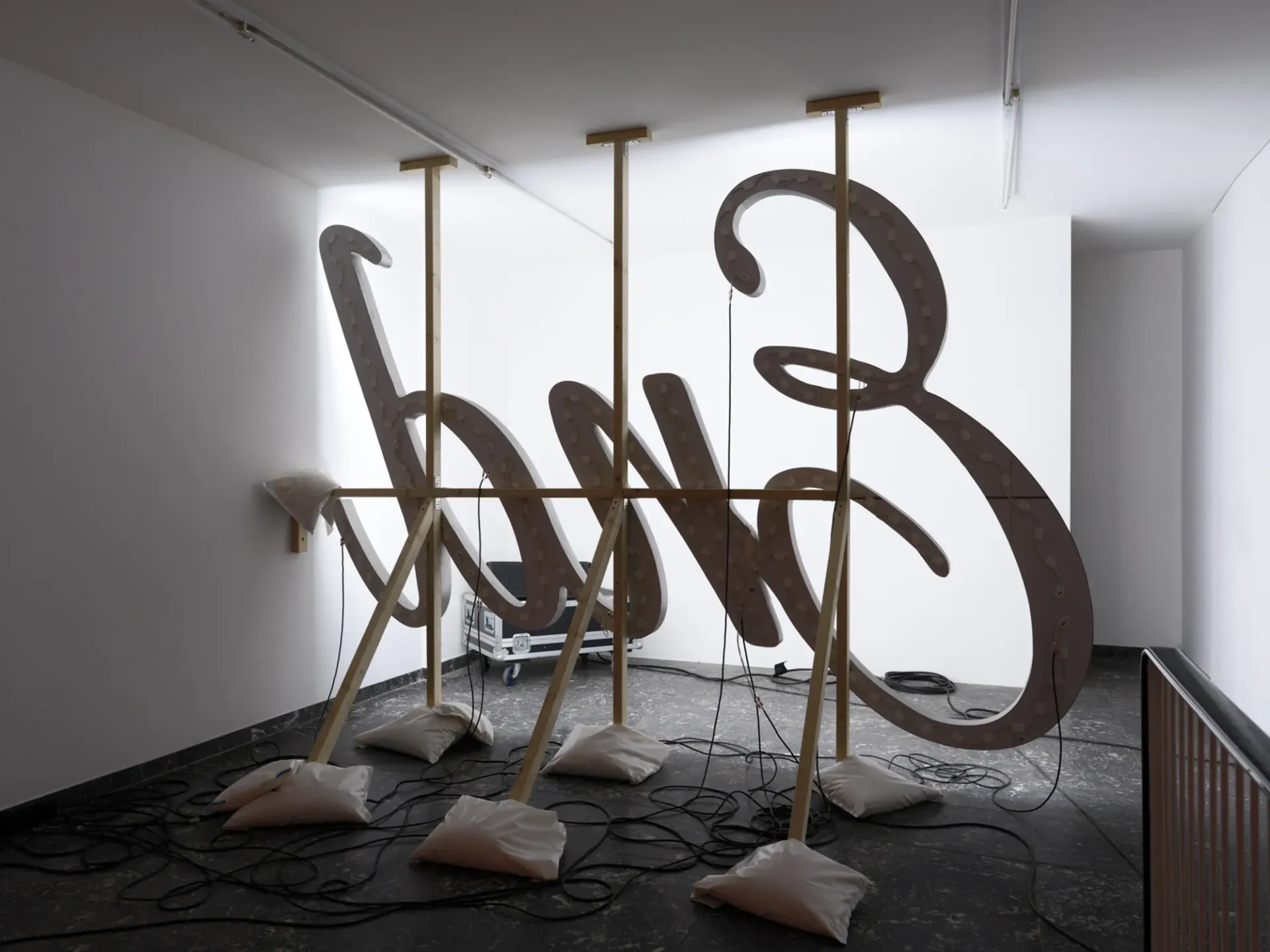 Banks Violette’s site-specific exhibition Wish You Were Here at TICK TACK, Antwerp, showing suspended illuminated letterforms with exposed wiring and weighted support