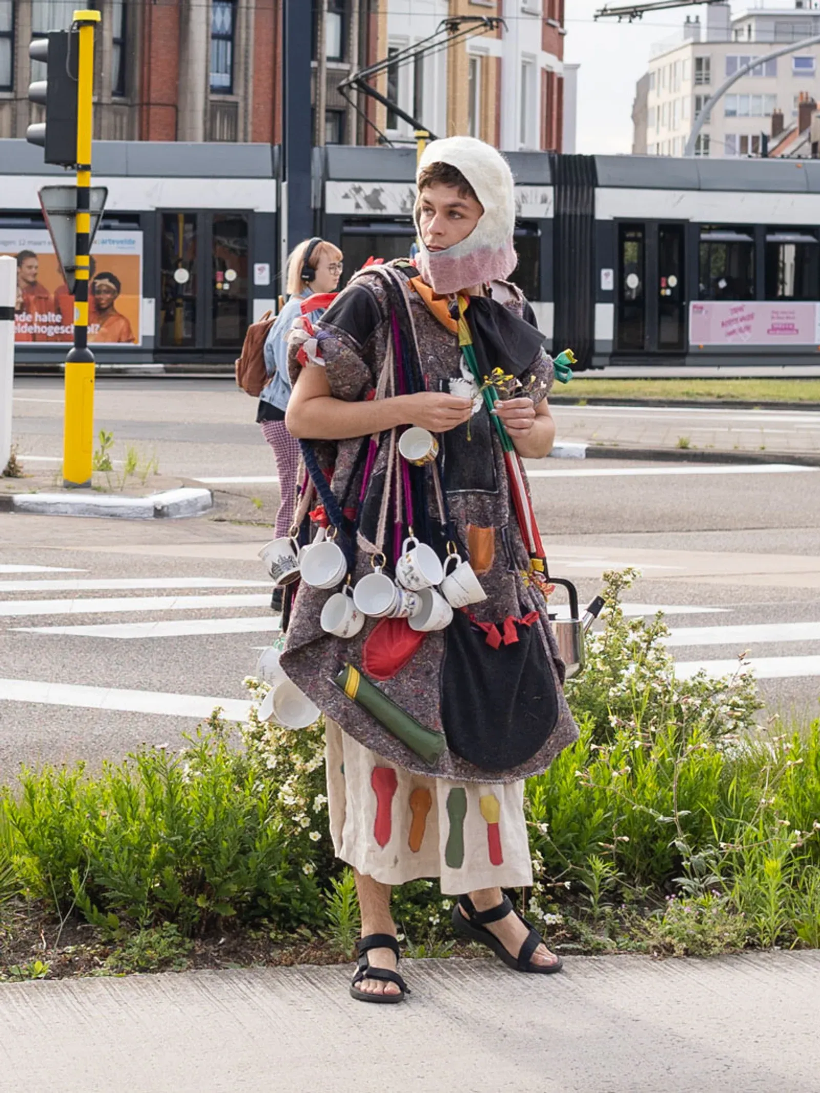 Pierre-Yves Delannoy, Willkommen bei den AGA (2024), performance participant wearing a handmade costume with cups and objects during a street performance.
