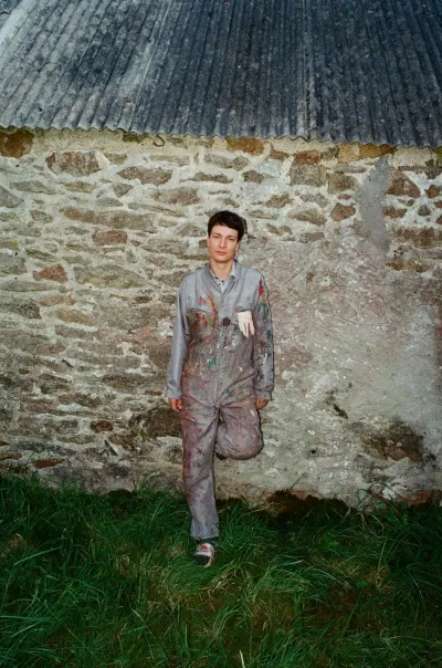 Portrait of Ruben Einsmann standing outdoors in paint-covered work clothes in front of a stone wall.