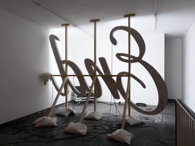 Banks Violette’s site-specific exhibition Wish You Were Here at TICK TACK, Antwerp, showing suspended illuminated letterforms with exposed wiring and weighted support